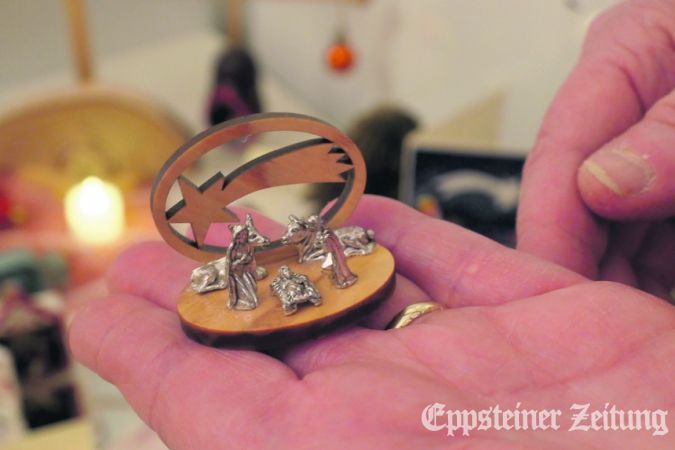 Die winzige Krippe aus Zinn auf einem Holzsockel passt auf eine Handfläche.