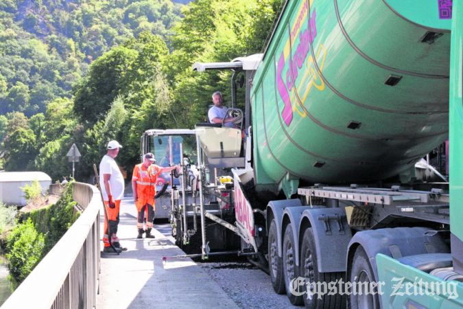 Bei langsamer Fahrt füllt der Lkw heißen Asphalt in den Asphaltfertiger. Der verteilt die Masse gleichmäßig auf dem Unterbau der Straße. Gleich danach verdichten Walzen diese Tragschicht.